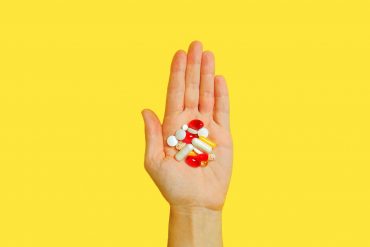 person with bunch medication pills on hand supplements